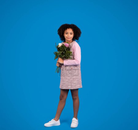 Photo for Smiling african american little girl with bouquet of flowers isolated on blue background, studio, full length. Holiday celebration, congratulation, childhood and children emotions - Royalty Free Image