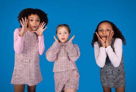 Photo for Shocked surprised glad multiethnic little girlfriends in casual have fun isolated on blue background, studio. Facial expression, children emotions, family, friendship and education, ad and offer - Royalty Free Image