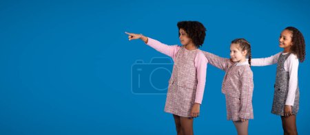 Téléchargez les photos : Positif diverses petites filles dans occasionnels ont du plaisir, pointant du doigt l'espace libre isolé sur fond bleu, studio. Offre pour l'éducation, divertissement ensemble, émotions des enfants - en image libre de droit