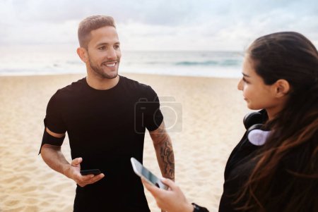 Photo for Jogging coaching. Sporty man and woman chatting before morning run on the beach of ocean, lady and guy holding smartphones and talking outdoors - Royalty Free Image