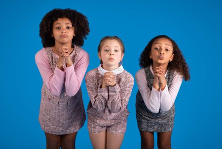 Téléchargez les photos : Petites filles internationales occasionnelles faire un geste pour prier, demander regarder la caméra isolée sur fond bleu, studio. Espoir, rêve, immense désir d'éducation à l'école, émotions des enfants - en image libre de droit