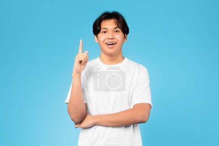 Photo for Aha. Cheerful Asian Teenager Guy Having Idea Pointing Finger Up Looking At Camera Posing Standing Over Blue Studio Background. Student Boy Experiencing Eureka Moment Having Inspiration - Royalty Free Image