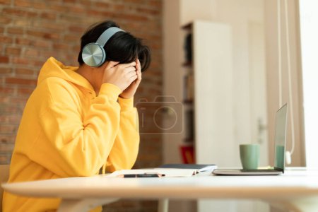Photo for Depressed Japanese Teen Boy Having A Hard Time Doing School Homework Online, Covering Face Sitting At Laptop At Home. Teen Age Depression And Difficulty Of Distance Education Concept - Royalty Free Image