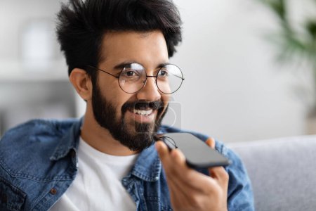 Photo for Handsome Young Indian Man Using Smartphone For Recording Voice Message, Smiling Millennial Eastern Man Holding Mobile Phone, Browsing Virtual Assistant Or Speaking With Loudspeaker Mode, Closeup - Royalty Free Image