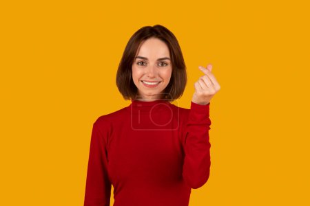Photo for Positive young woman showing money gesture. Portrait of positive lady smiling and showing give me money gesture, asking for payment. Studio shot isolated on orange background, copy space - Royalty Free Image