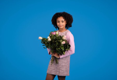 Photo for Greeting happy birthday. Positive african american little curly kid with bouquet of flowers enjoy celebration isolated on blue background, studio. Holiday congratulation, childhood and emotions - Royalty Free Image