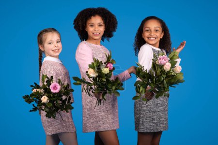 Photo for Glad positive multiethnic little girls with bouquets of flowers have fun, isolated on blue background, studio. Greeting, holiday celebration, congratulation, childhood and emotions children - Royalty Free Image