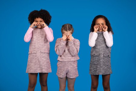 Photo for Sad offended international little girls in casual crying, isolated on blue background, studio. Fright, stress, fear and problems in school, childhood and children emotions - Royalty Free Image