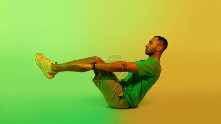 Photo for Workout. Black Sportsman Doing V-Ups Abdominal Exercise Sitting On Floor Over Green Studio Background. Sporty Guy Flexing Abs Doing Crunches Holding Raised Legs And Outstreched Arms - Royalty Free Image