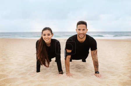 Téléchargez les photos : Couple heureux en tenue de sport ne poussent ou planche sur la plage de l'océan, l'exercice à l'extérieur et souriant à la caméra. Relation, soins de santé, mode de vie actif - en image libre de droit