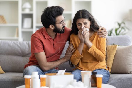 Photo for Care And Support. Loving Indian Man Caring About His Ill Wife Suffering Seasonal Flu At Home, Caring Eastern Male Embracing And Comforting Spouse, Sick Woman Blowing Nose To Napkin, Closeup - Royalty Free Image