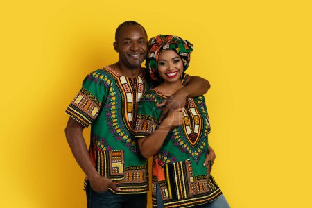Téléchargez les photos : Beau joyeux couple heureux afro-américain portant des costumes traditionnels posant ensemble sur fond de studio jaune, étreignant et souriant à la caméra, espace de copie. Mariage, relations - en image libre de droit