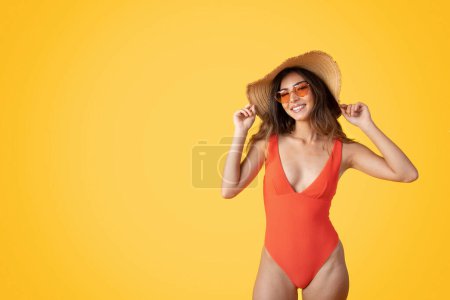Photo for Happy young european slim woman in swimsuit, hat and sunglasses enjoy rest , trip at spare time, isolated on orange studio background, copy space. Beach holidays, vacation at summertime - Royalty Free Image