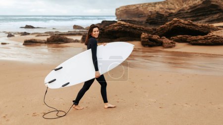 Photo for Recreation and hobby concept. Happy woman being in high spirit after surfing, walking with surfboard and smiling at camera, enjoying extreme sport, panorama, copy space - Royalty Free Image