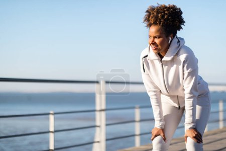 Foto de Respirando. Retrato de una joven atleta negra descansando después de trotar al aire libre, una mujer afro-americana deportiva motivada haciendo una pausa durante el entrenamiento exterior, relajándose después del entrenamiento físico - Imagen libre de derechos