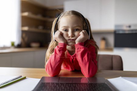 Photo for Boring Content. Pov shot of upset little girl in wireless headphones looking at laptop screen at home, bored preteen female child sitting at desk and using computer, webcam point of view - Royalty Free Image
