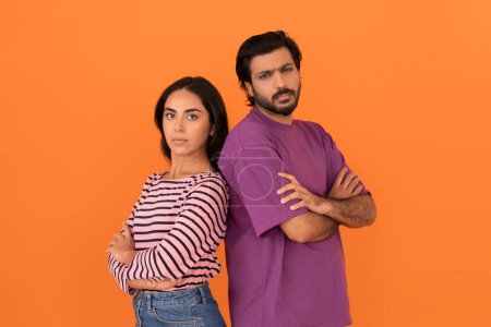Photo for Break up, difficulties in relationships. Upset young indian man and woman wearing casual outfit standing back to back, looking at camera, orange studio background, copy space - Royalty Free Image