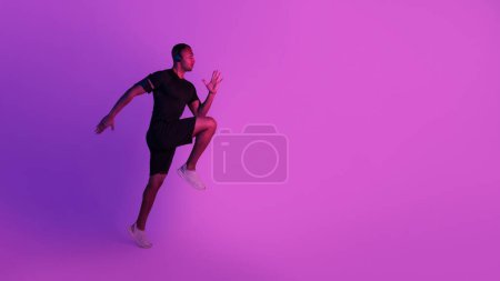 Photo for Workout. Sporty African American Guy Exercising Wearing Headphones Doing Elbow To Knee Crunches, Standing Looking Aside At Free Space Over Purple Studio Background. Fitness Training. Panorama - Royalty Free Image