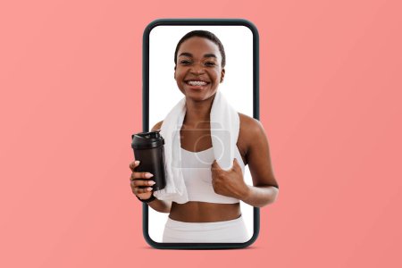Photo for Happy millennial black woman with towel and bottle of water or protein shake ready for workout on phone isolated on pink studio background. App for training, body care, sports blog - Royalty Free Image