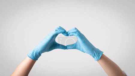 Photo for Emphasizing compassion in healthcare. Woman doctor wearing protective gloves, forming a heart shape with her hands, symbolizing the vital role of empathy in providing high-quality patient care - Royalty Free Image