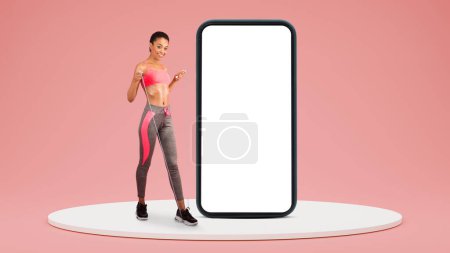 Photo for Glad young black lady in sportswear do exercises with jump rope near phone on platform isolated on pink studio background, collage. App for fit, workout, weight loss and health care, sports blog - Royalty Free Image