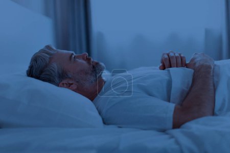 Photo for Insomnia, sleeping disorder concept. Sleepless unhappy grey-haired middle aged man wearing pajamas lying in bed late at night, watching ceiling, cant sleep, side view, copy space - Royalty Free Image