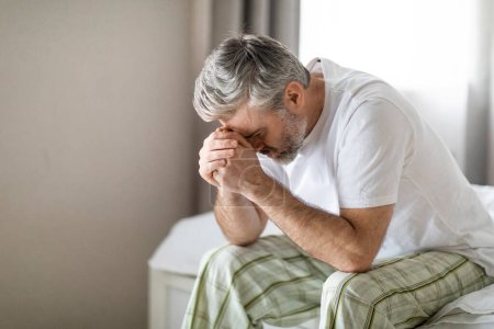 Photo for Upset broken grey-haired middle aged man wearing pajamas sitting on bed at home in the morning, leaning on his hands, crying, suffer from midlife criss, experience difficulties in life, copy space - Royalty Free Image