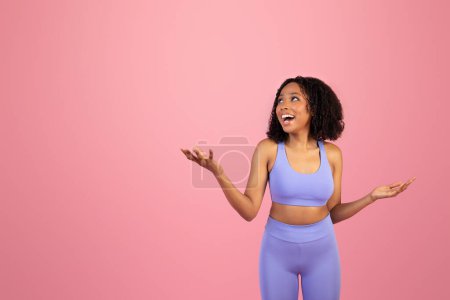 Photo for Surprised glad millennial african american lady in sportswear with open mouth hold empty space in hands isolated on pink background, studio. Sports, ad and offer, pilates, fitness and body care - Royalty Free Image