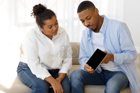 Photo for Online therapy app, modern technologies in psychotherapy. Young black man therapist showing chubby hispanic lady patient digital tablet with blank screen during session, mockup, clinic interior - Royalty Free Image