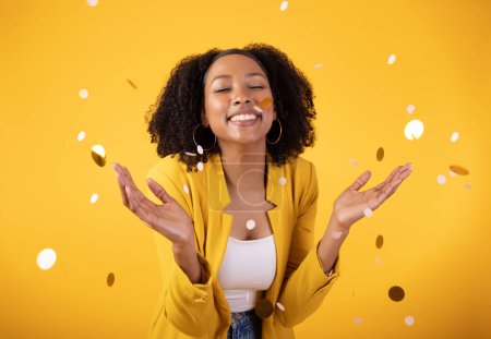 Photo for Festive mood. Excited pretty black lady throwing confetti, celebrating holiday isolated on yellow background, studio shot. Ad and offer for huge party, New Year - Royalty Free Image