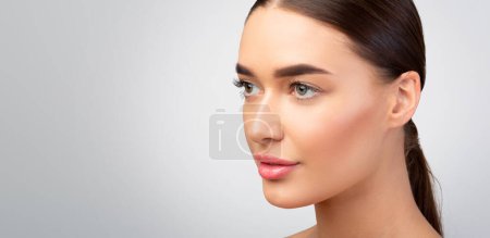 Photo for Facial Skincare Offer. Gorgeous Young Lady With Natural Makeup And Perfect Face Skin Looking Aside At Empty Space For Text, Advertising Cosmetic Products On Gray Background. Studio Shot, Panorama - Royalty Free Image