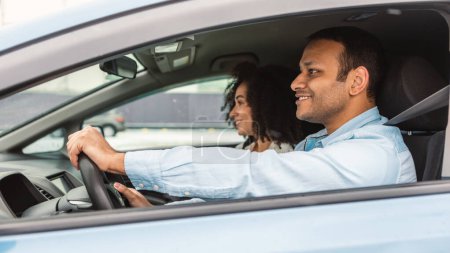 Photo for Side View Shot Of Arabic Spouses Driving New Auto, Man Posing WIth Hands On Wheel Sitting In Drivers Seat Of The Vehicle. Couple Enjoying Car Ride Together. Panorama, Selective Focus - Royalty Free Image