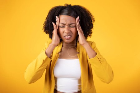 Photo for Unhappy african american lady pressing her hands to temples, suffering from headache and migraine, standing on yellow background. Stress, pressure, depression and health problems - Royalty Free Image