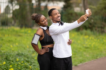 Téléchargez les photos : Joyeux jeune couple afro-américain prendre selfie sur smartphone dans le parc en plein air. Photo pour blog sportif et réseaux sociaux, soins du corps, entraînement en ville ensemble, mode de vie actif et perte de poids - en image libre de droit