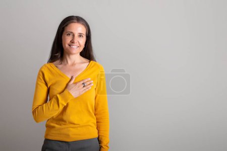 Photo for Cheerful pretty caucasian elderly lady puts her hand to chest, make thanks gesture on gray studio background, copy space. Great news, thanks sign, ad and offer, people emotions - Royalty Free Image