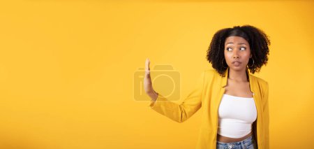 Foto de Señora afroamericana seria haciendo gesto de stop con la mano y mirando a un lado el espacio libre aislado sobre fondo amarillo, panorama. Señal de espacio personal y decir no concepto - Imagen libre de derechos