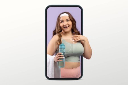 Photo for Smiling young caucasian lady plus size in sportswear with bottle of water on big smartphone screen isolated on white studio background. Body care app, blog for weight loss and fit - Royalty Free Image
