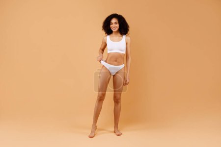 Photo for Full body length shot of fit black lady with slim body posing in underwear, young female with perfect sporty figure and flat abdomen standing isolated on beige studio background, copy space - Royalty Free Image