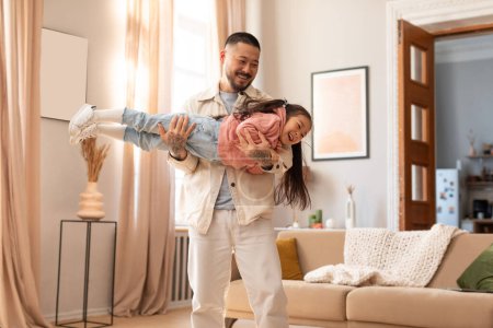 Photo for Joyful Bonding. Happy Japanese Dad Lifting Little Baby Daughter In Air, Playing And Having Fun Enjoying Playtime Together At Home. Weekend With Funny Loving Daddy Concept - Royalty Free Image
