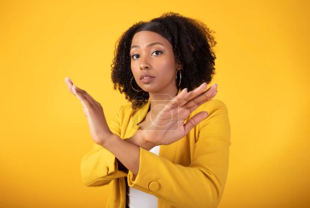 Téléchargez les photos : Concept de rejet et d'avertissement. Mécontente dame noire croisant les mains en geste de désapprobation rejetant quelque chose, debout sur fond jaune. Arrête ça. - en image libre de droit
