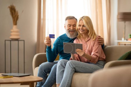 Photo for Secure Online Transactions. Happy Senior Couple Shopping Via Digital Tablet Holding Credit Card, Making Payment Together Sitting On Sofa At Home. Ecommerce Offer Advertisement - Royalty Free Image