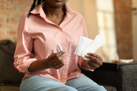 Photo for Female period and intimate hygiene. Young black woman holding tampon vs clean menstrual pads, choosing between feminine hygiene products, free space - Royalty Free Image