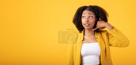 Téléchargez les photos : Rappelle-moi. Jeune femme noire montrant un panneau téléphonique à la main, regardant de côté l'espace de copie, isolée sur fond de studio jaune. Flirt, communication, émotions des gens - en image libre de droit