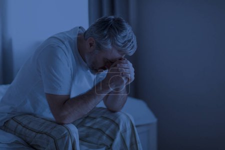 Photo for Insomnia, sleeping disorder concept. Sleepless depressed middle aged man wearing pajamas sitting on bed at home, touching his head, cant sleep, awake late at night, copy space - Royalty Free Image
