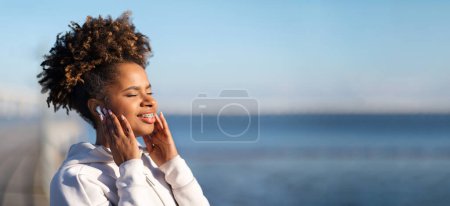 Photo for Beautiful Young Black Female Enjoying Favorite Music In Wireless Earphones While Training Outdoors, Smiling African American Woman In Sportswear Standing With Closed Eyes, Listening Audio Podcast - Royalty Free Image