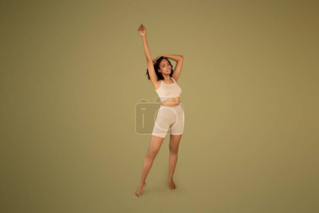 Photo for Smiling slim millennial curly african american lady in sportswear enjoy workout isolated on beige background, studio. Body care, sport ad and offer, fitness, pilates and yoga - Royalty Free Image