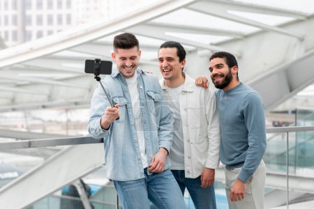 Photo for Airport Entertainment. Cheerful Tourists Men Trio Making Selfie On Phone And Making Video For Travel Blog Having Fun In Terminal Indoor, Waiting For Flight And Sharing Vacation Journey Moments - Royalty Free Image