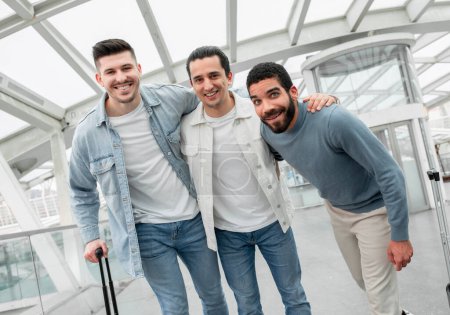 Photo for Ready for Boarding. Tourists Men Trio Hugging Posing With Luggage In Modern Airport Lounge. Guys Traveling Enjoying Vacation With Friends And Waiting For Their Flight. Travel Tickets Offer - Royalty Free Image