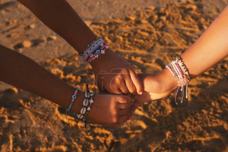 Foto de Amistad femenina. Primer plano de tres amigos sosteniendo las manos usando pulseras lindas y pulseras sobre arena colgando en la playa juntos, disfrutando del día de verano en el mar al aire libre. Tiro recortado - Imagen libre de derechos