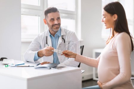 Photo for Pregnancy nutrition. Male specialist giving vitamins or supplements to young pregnant woman, doctor prescribing pills for treatment. Female patient receiving tablets from doctor - Royalty Free Image